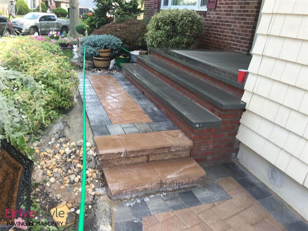 Front steps and walkway beside a brick house, with wet pavement and landscaped garden edging.