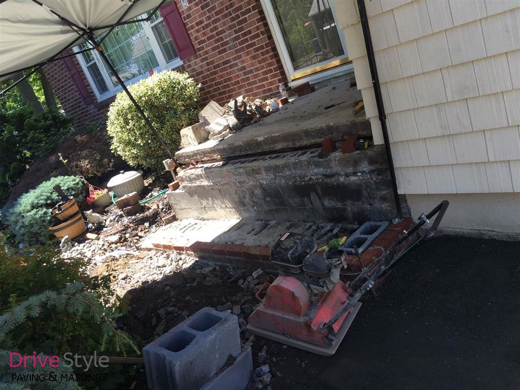 Garden tiller parked by brick steps beside a house with a shingled exterior