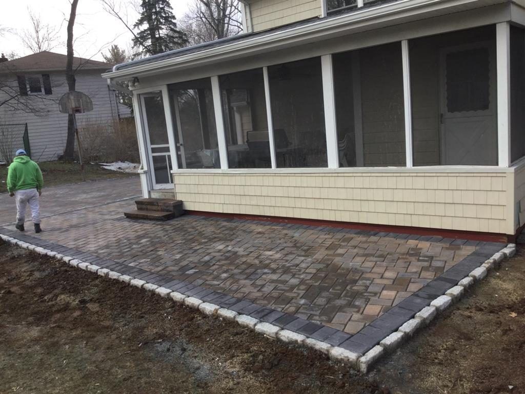 House with screened porch and paved walkway under construction, with a worker in a green jacket nearby
