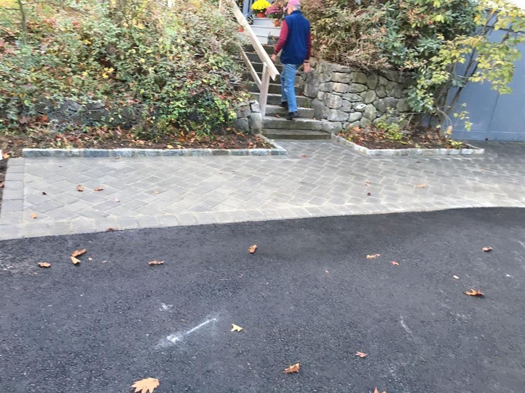 Person in a red jacket climbing stone steps beside a retaining wall and blue building.