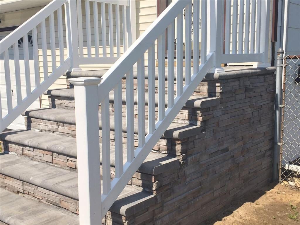 White staircase with railings beside a gray stone retaining wall outdoors