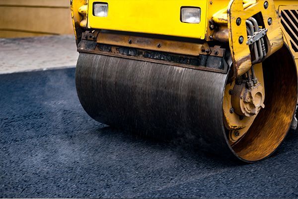 Yellow road roller compacting dark asphalt on a street construction site