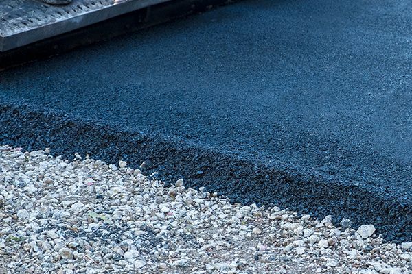 Freshly paved dark asphalt edge beside a gravel shoulder