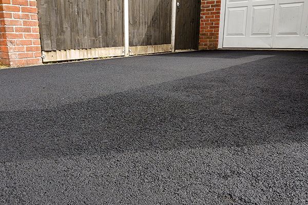 Freshly paved dark asphalt driveway beside a brick garage and white door
