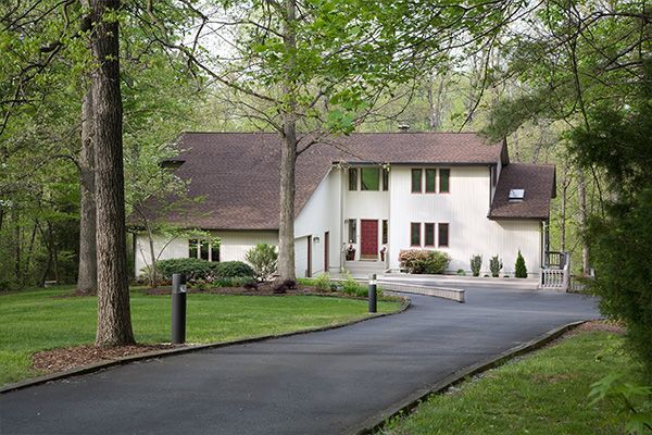 White house with a curved driveway, surrounded by green trees and lawn.