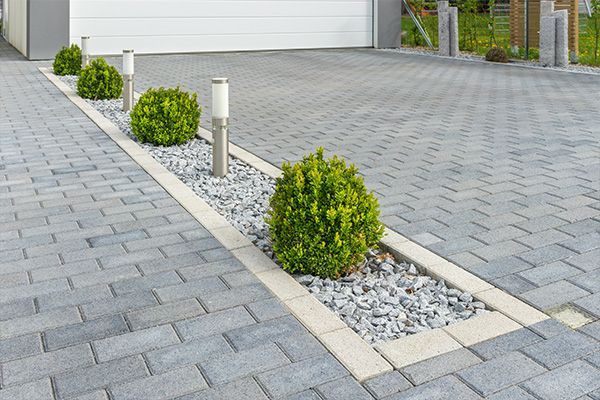 Landscaped driveway with gray pavers, white gravel strip, and small green shrubs