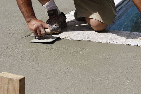 Person smoothing wet concrete beside a blue-striped curb with a trowel