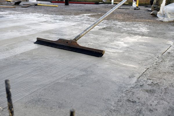 A worker uses a wide squeegee to smooth wet concrete on a construction surface.