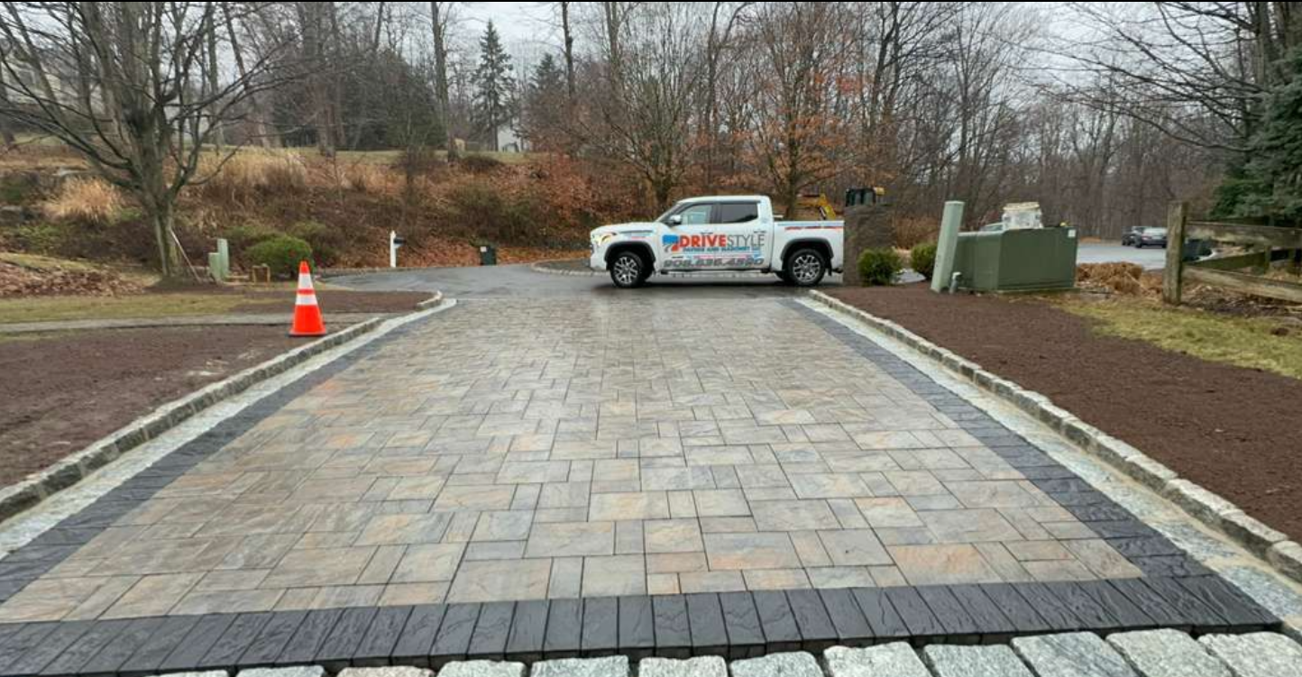 Workers paving a residential driveway, with one person operating a machine and others spreading asphalt.