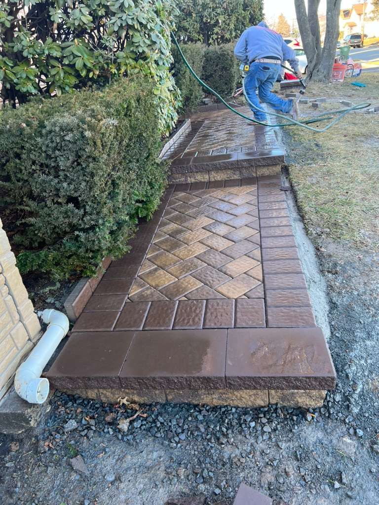 Worker installing a brick walkway beside a hedge in a yard