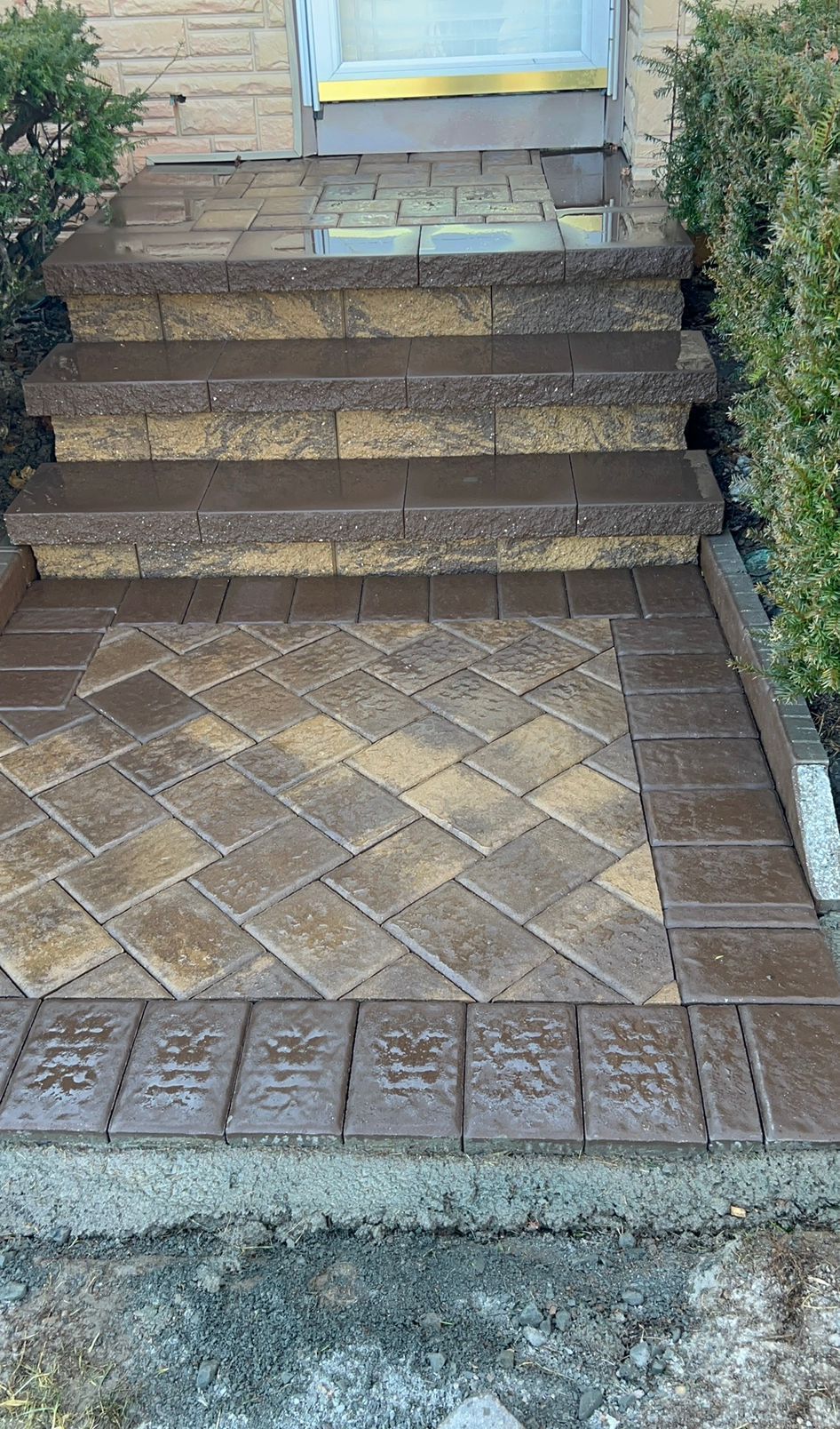 Front entrance with brick steps, tiled landing, and shrubs beside a doorway