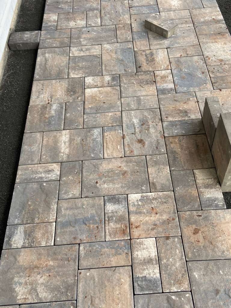 Uneven gray stone paver walkway with a narrow drainage strip on the left and a raised curb on the right