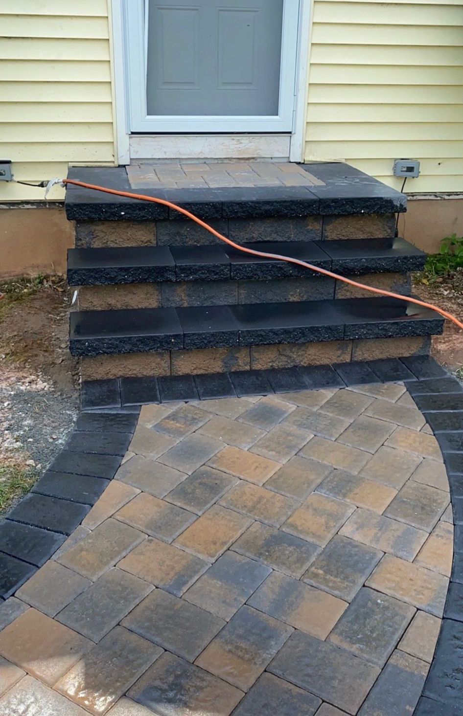 Front steps with a large crack in the walkway, cord stretched across them, leading to a house door