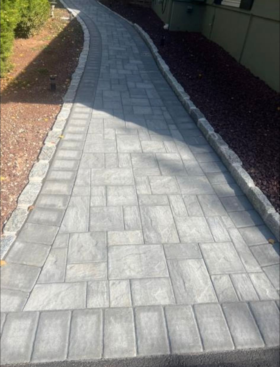 Curving gray paver walkway beside a building, bordered by mulch and edging stones.