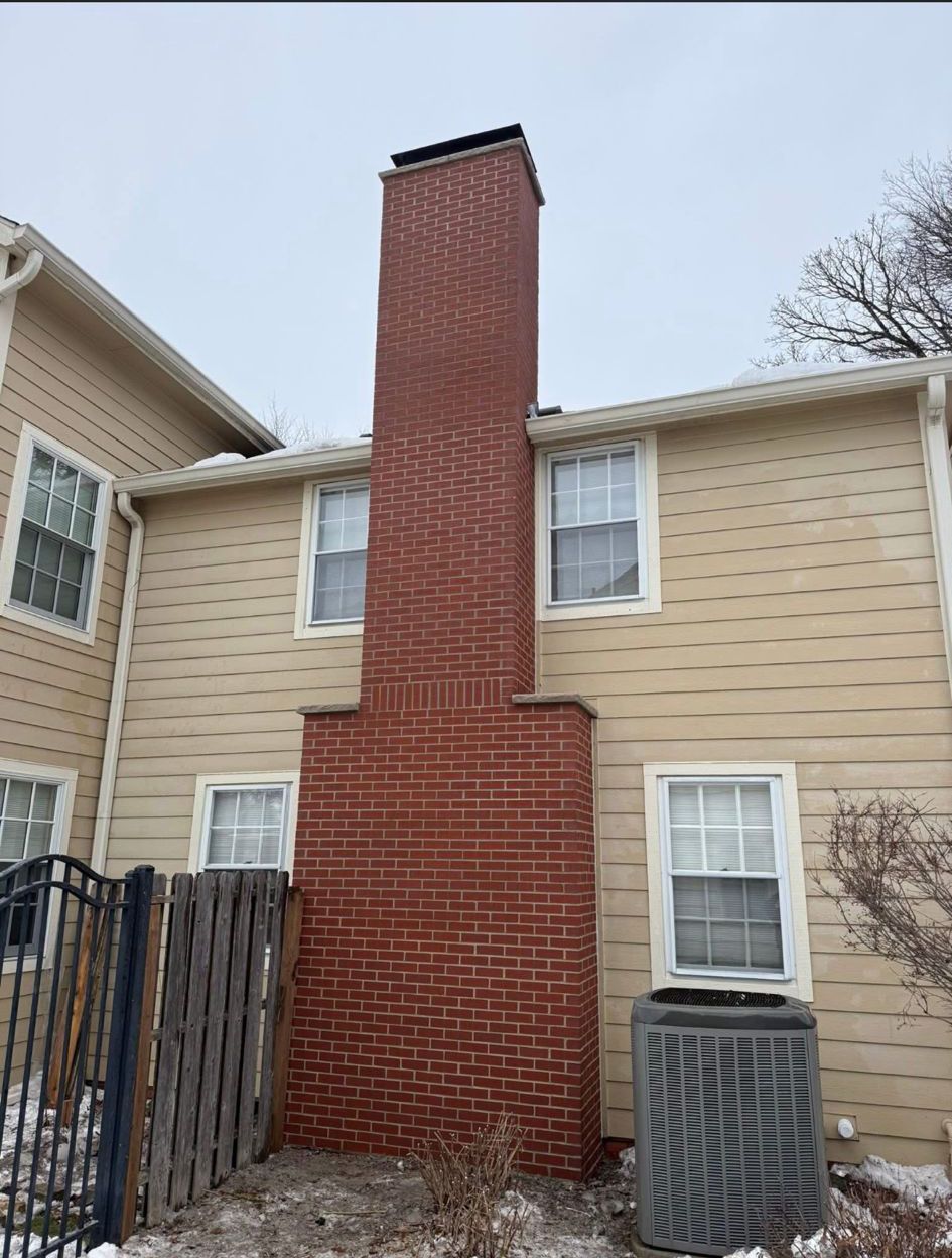Brick chimney on a beige townhouse exterior beside a window and air conditioner unit