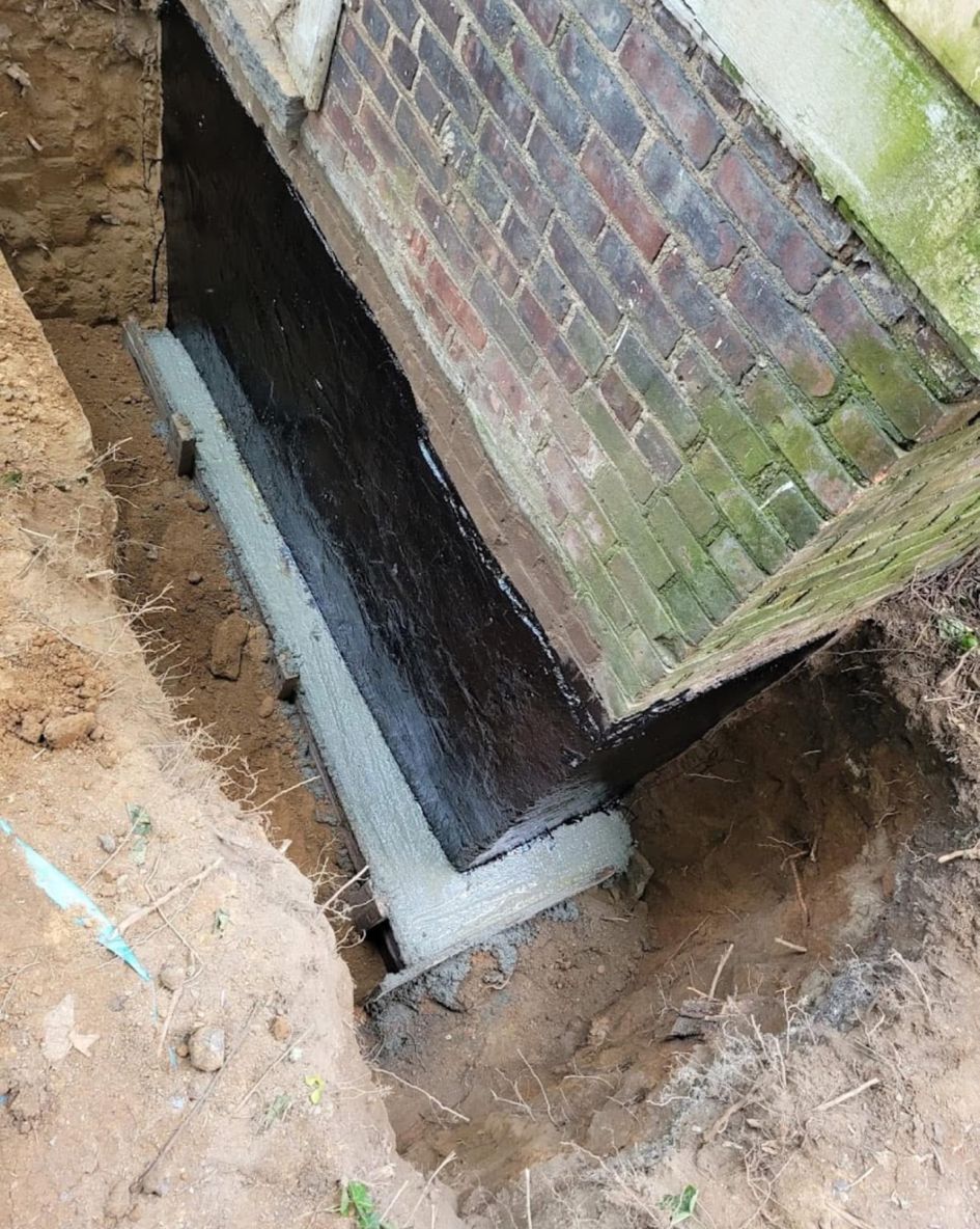 A basement window well beside a brick wall, with exposed soil and a concrete ledge.