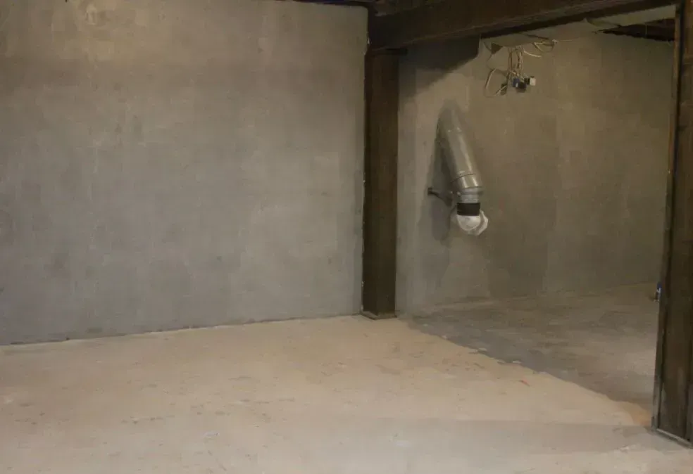 Empty unfinished room with bare concrete walls, floor, and a small metal vent or duct on the right.