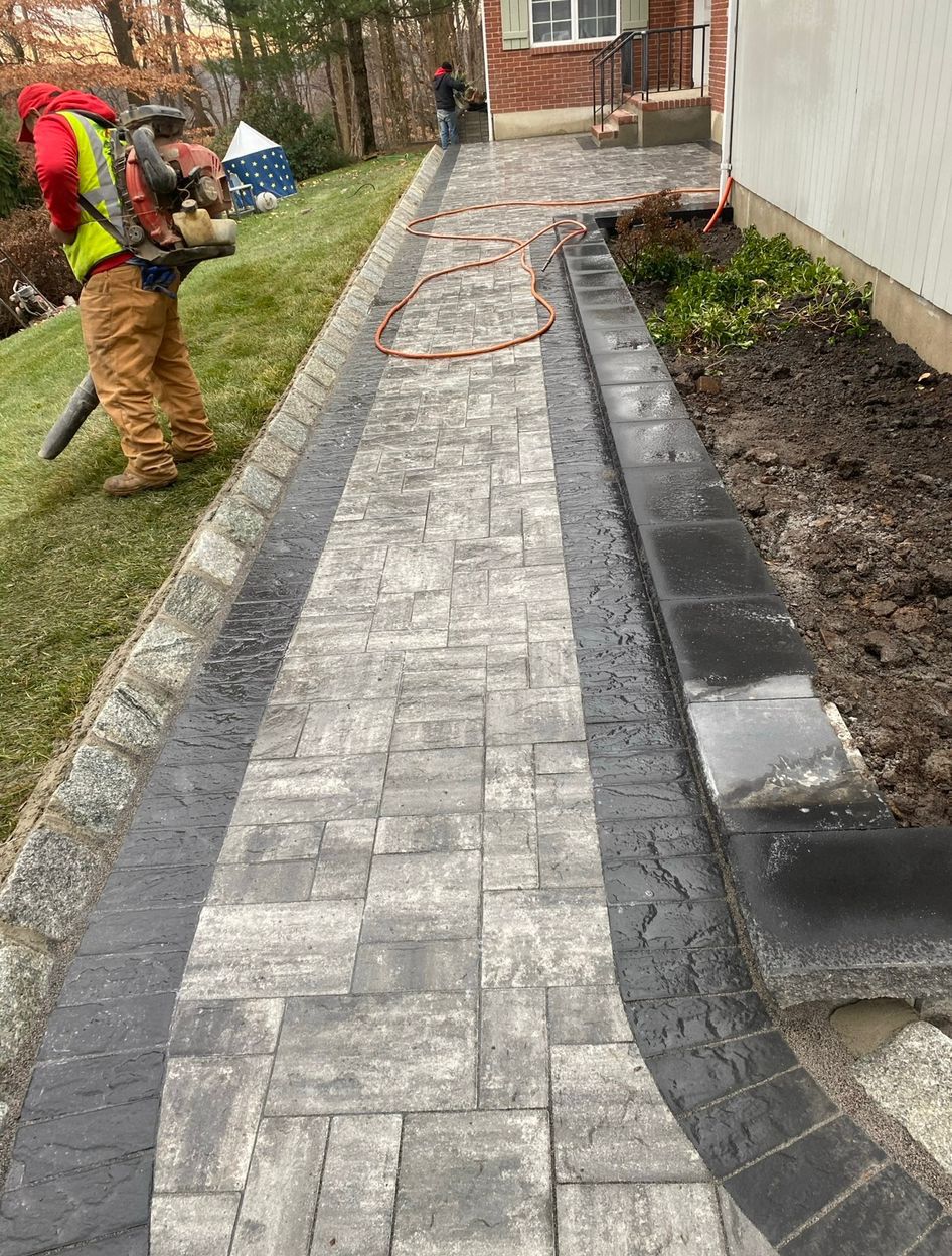Worker blowing leaves beside a newly paved brick walkway along a house