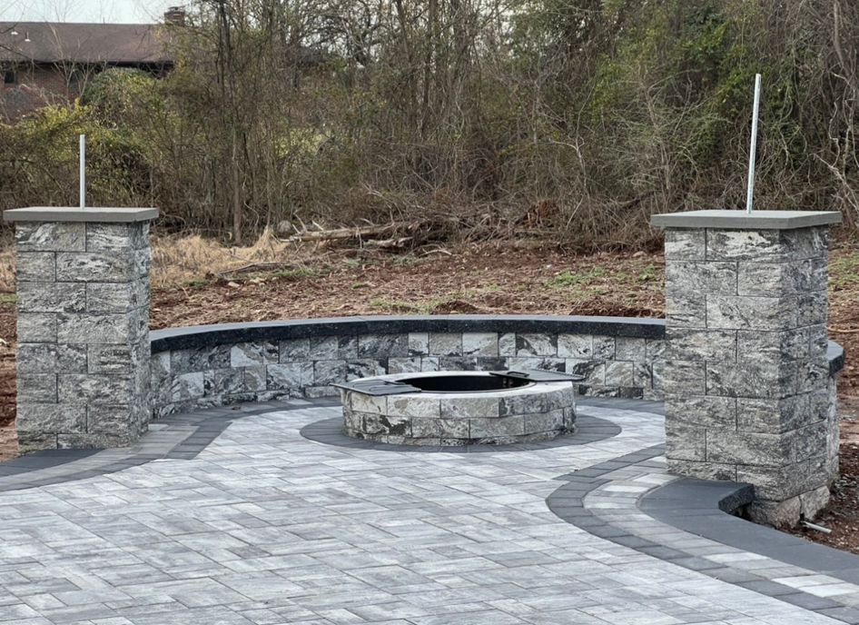 Stone patio with built-in circular fire pit and curved bench seating between two pillars outdoors