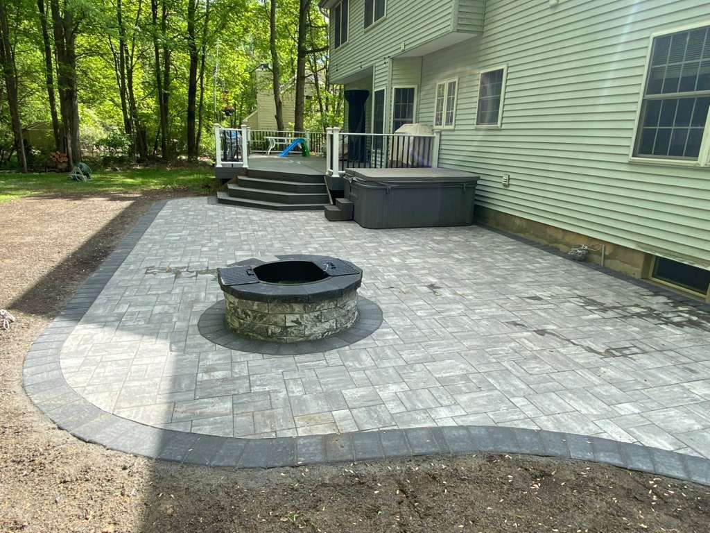 Backyard patio with stone pavers, circular fire pit, steps, and a house exterior