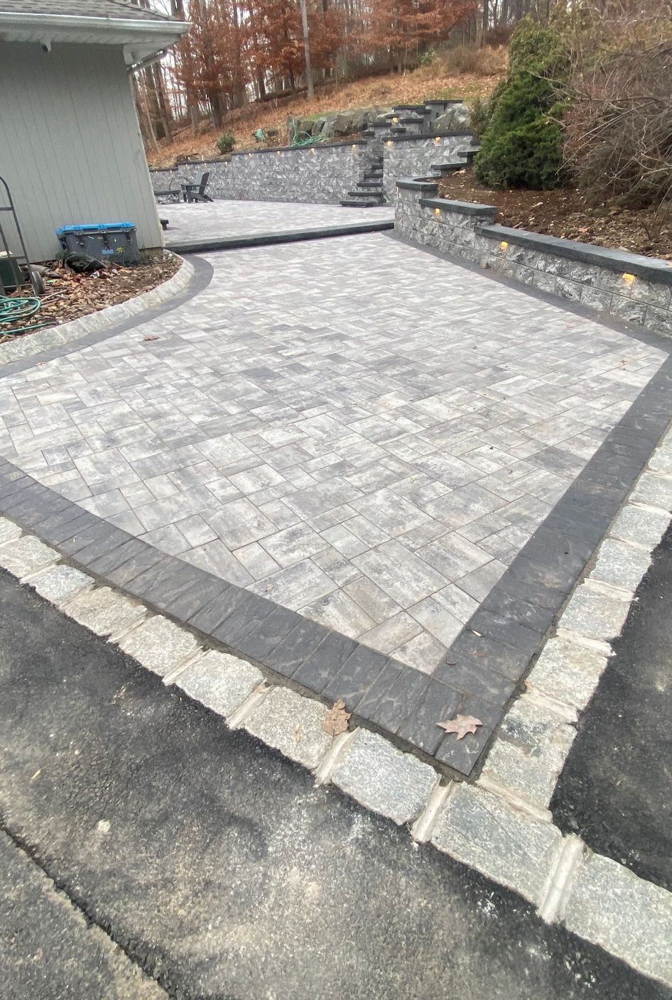 Stone-paver patio with retaining walls and a sloped landscaped yard