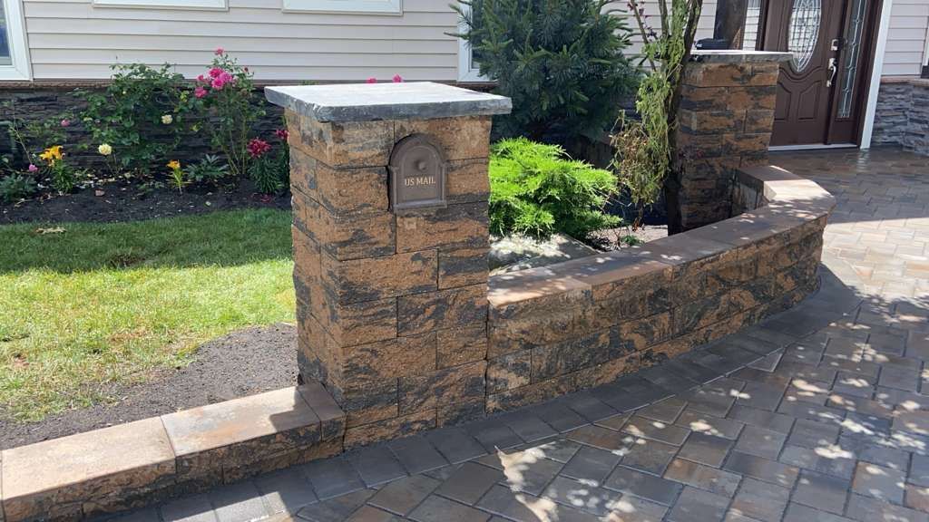 Stone mailbox and low retaining wall beside a driveway and house entrance, with snow on top.