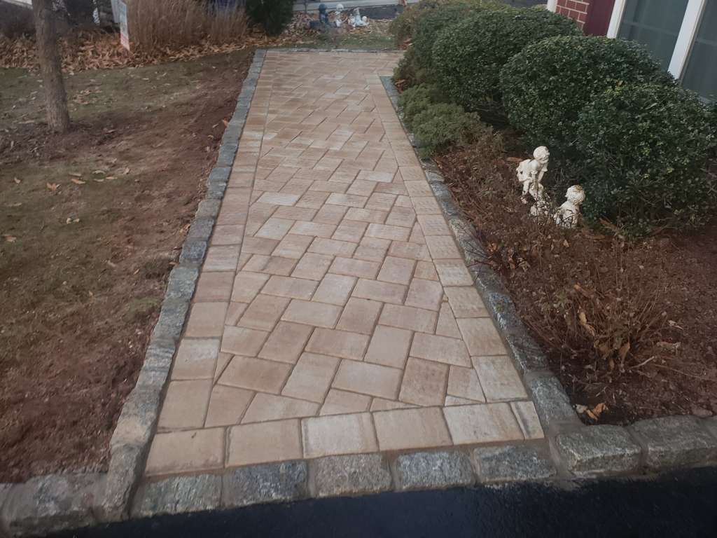Brick walkway bordered by gray pavers, shrubs, and mulch in a landscaped garden.