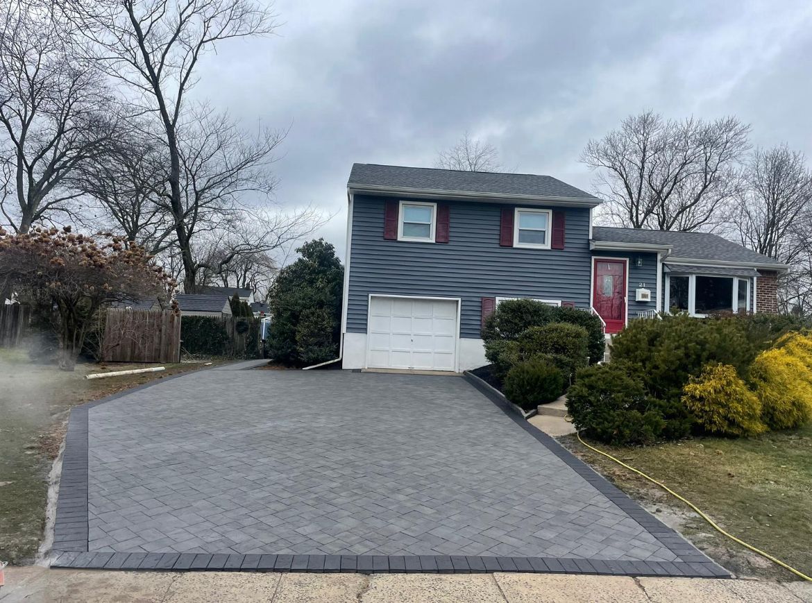 Blue two-story house with white garage, red door, and wide paved driveway in a wintery suburban yard