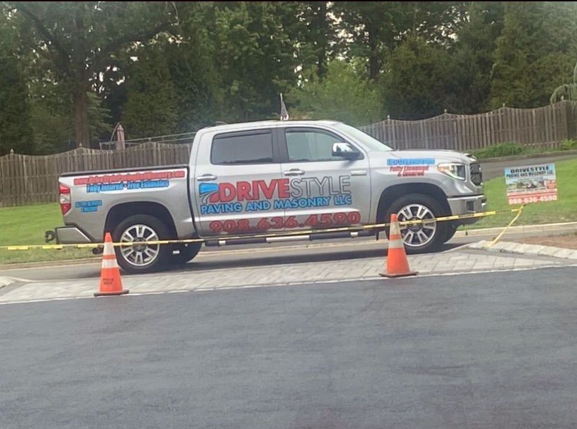 White pickup truck with company decals parked behind orange cones on a street, near a sidewalk and trees