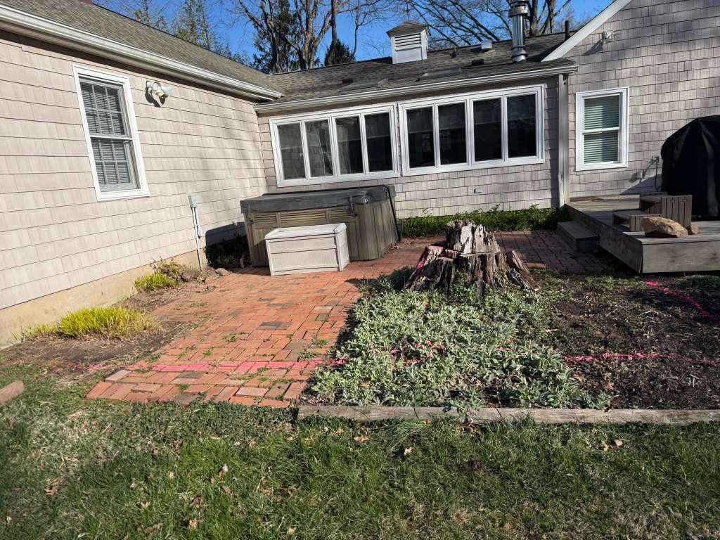 Backyard patio with brick path, raised garden bed, hot tub, and a house with windows