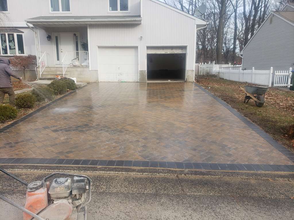 Freshly paved driveway leading to a white garage and house entrance, with a cement mixer in the foreground