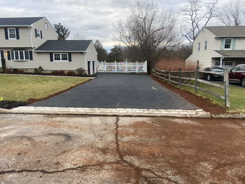Driveway with fresh black asphalt leading to a white fence between two suburban houses.