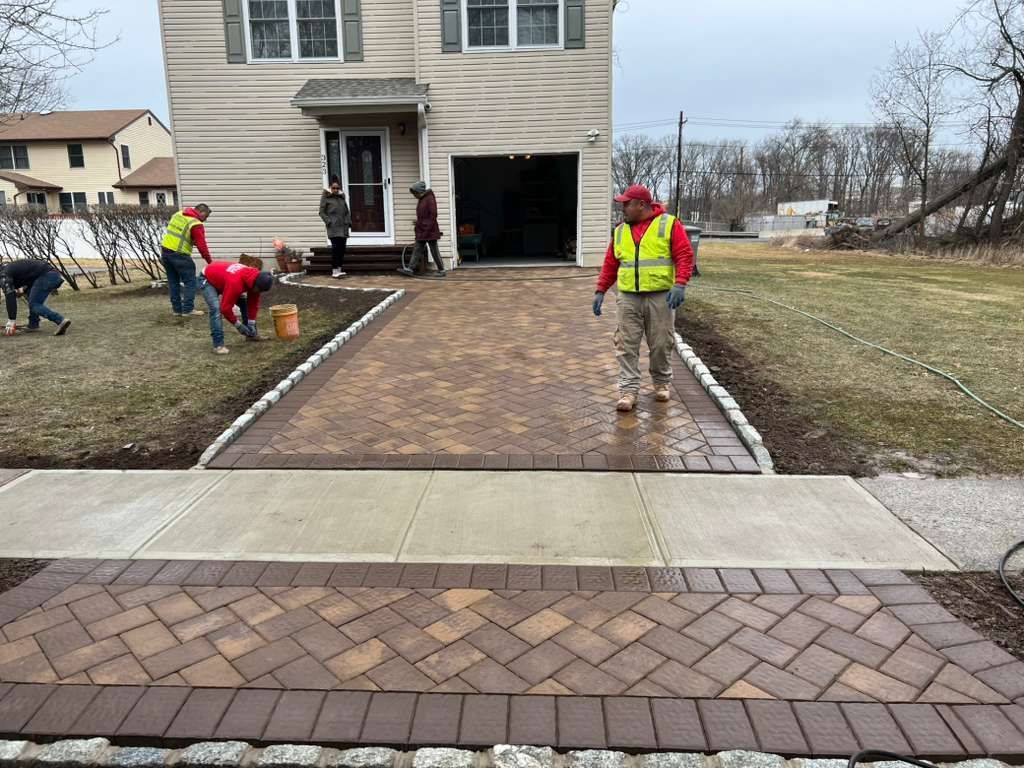 Workers install a brick walkway in front of a house on an overcast day.