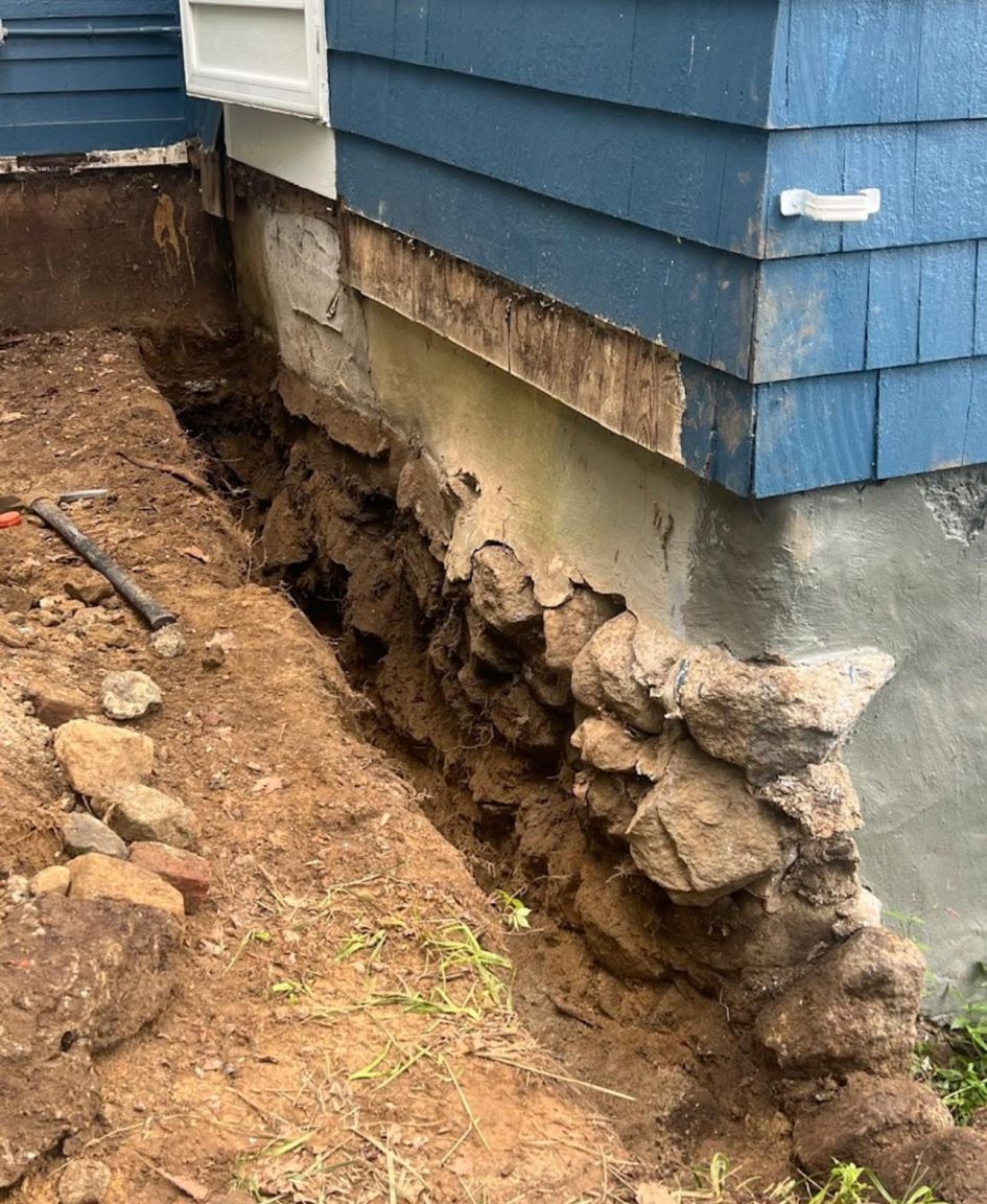 Excavated soil trench exposing foundation damage beside a blue house exterior