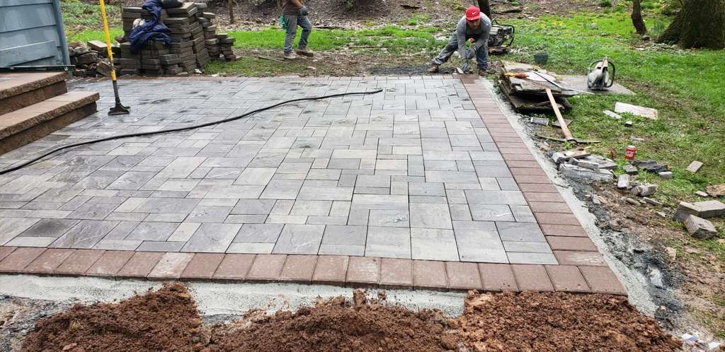 New brick-paved path under construction beside a muddy road, with workers in the background