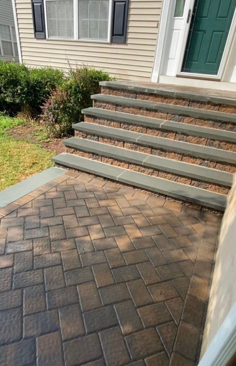 Brick patio leading to front steps and a green door on a house exterior