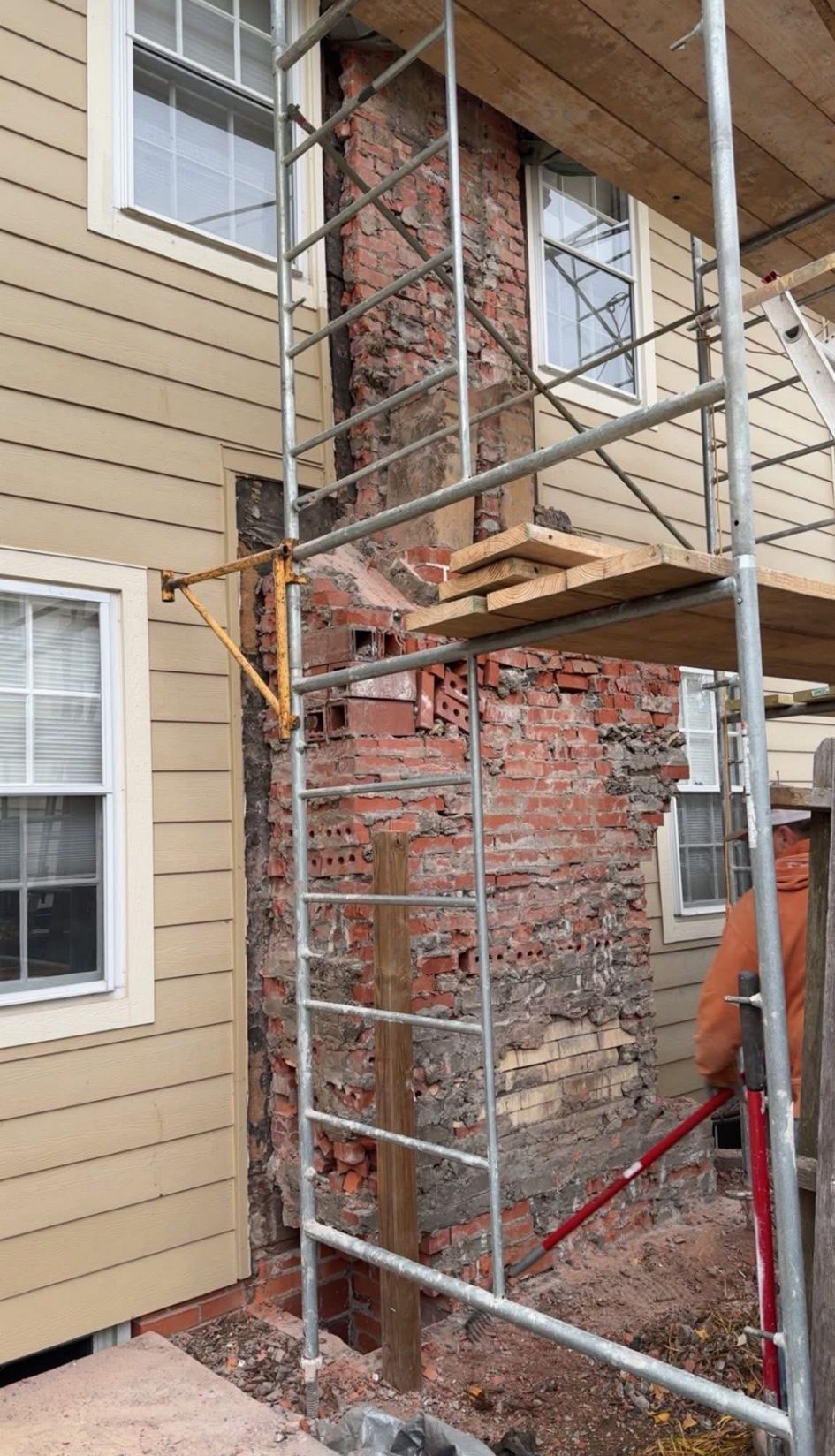 Scaffolding around a partially exposed brick wall beside beige siding during exterior renovation