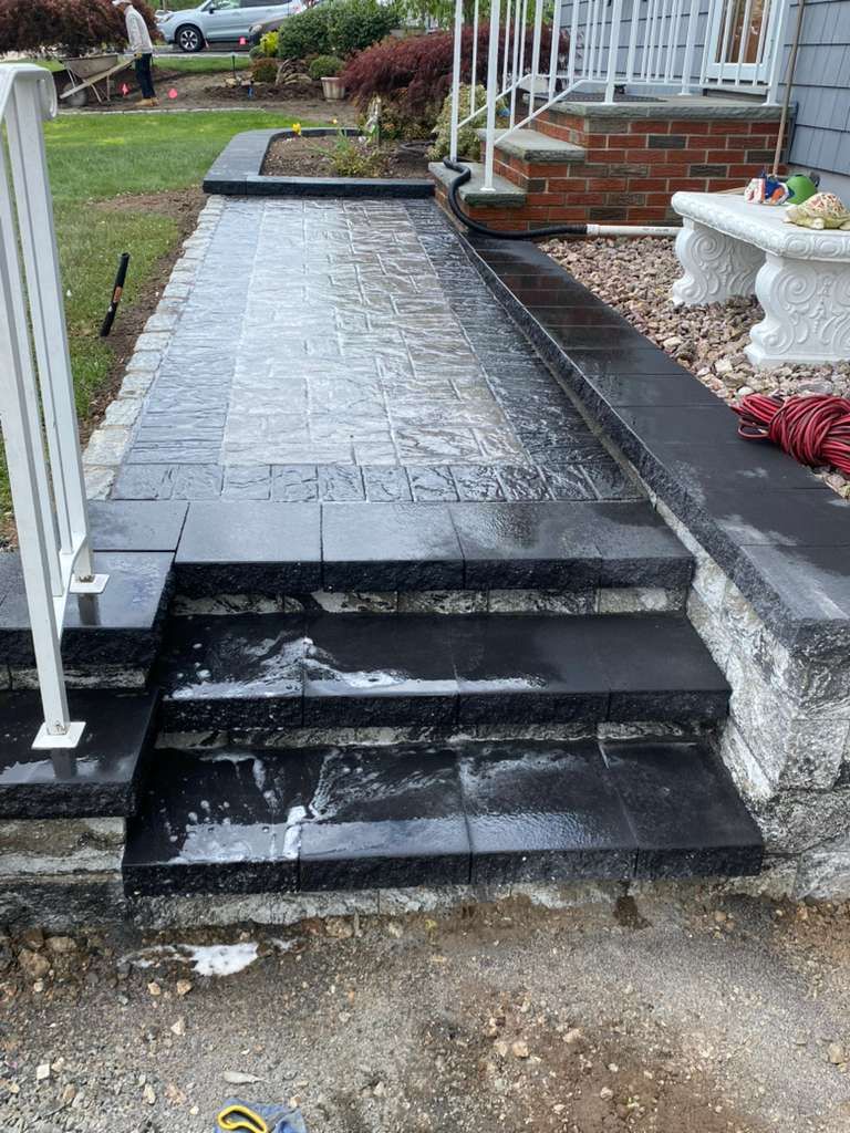 Black tiled front walkway with steps and a white railing leading to a brick house entrance.