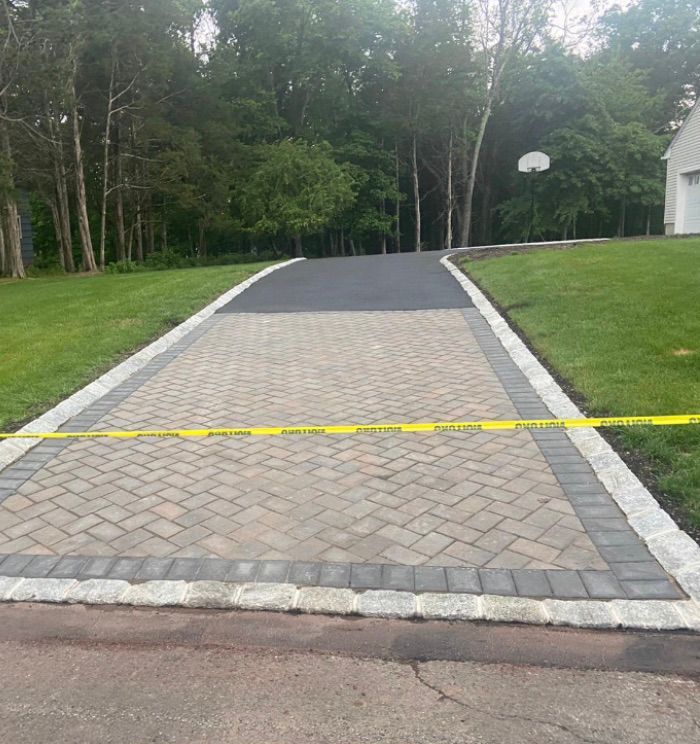 Paved driveway with a yellow caution tape across the front, bordered by grass and trees.
