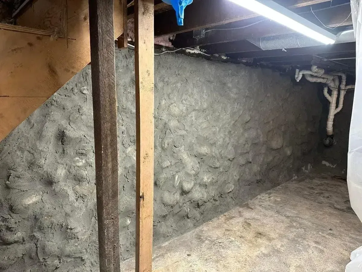 Damp basement crawlspace with concrete walls, exposed beams, and a low ceiling with fluorescent lighting