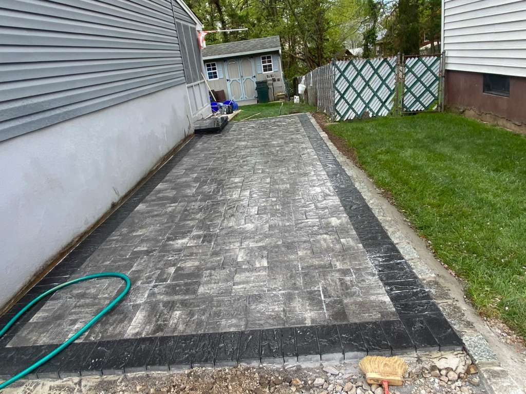 Concrete driveway beside a house, with a garden hose on the left and a grassy yard on the right.