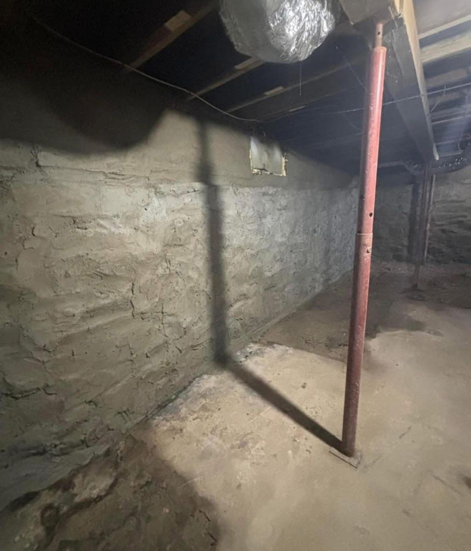 Dim basement with stone walls, exposed beams, and a red support pole on a dirt floor.