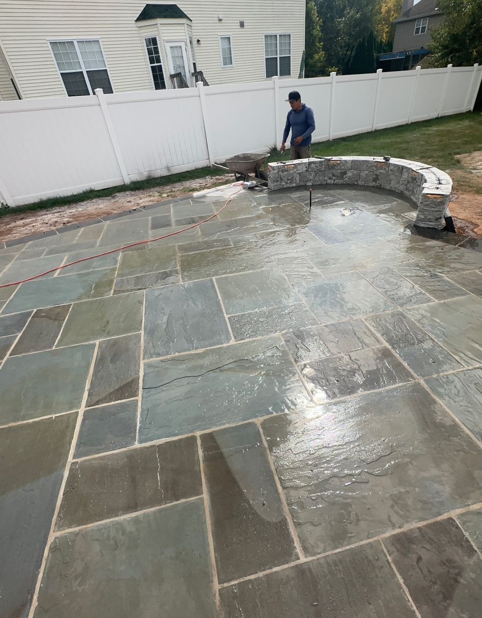 Wet stone patio with a curved bench and a person near a white fence in a backyard