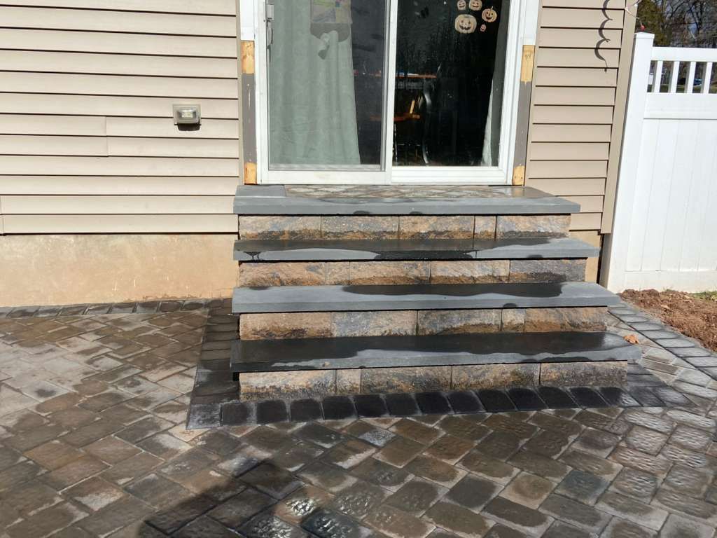 Stone front steps leading to a house entrance with beige siding and a white side gate