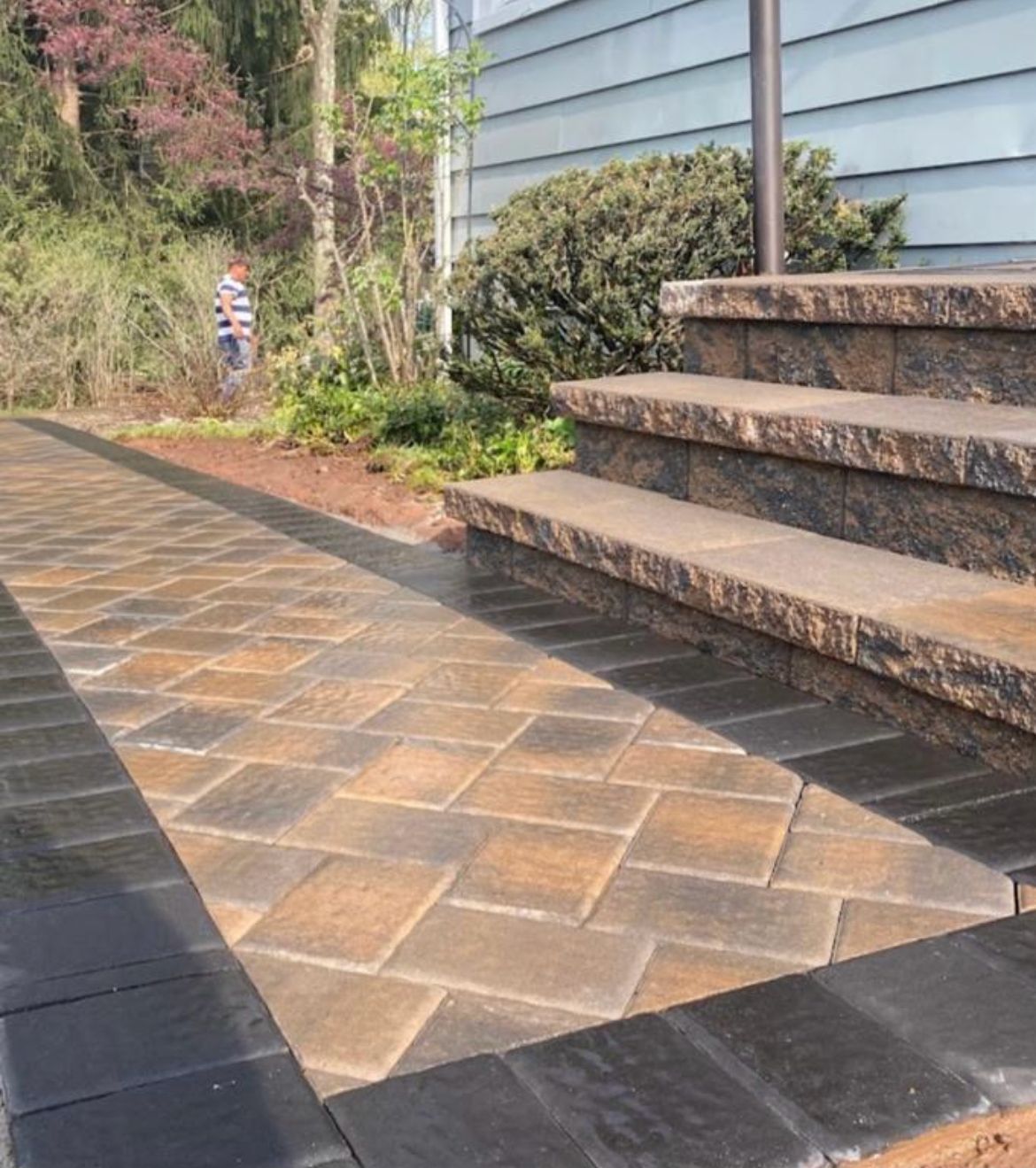Stone steps beside a blue house and paved walkway in a landscaped yard