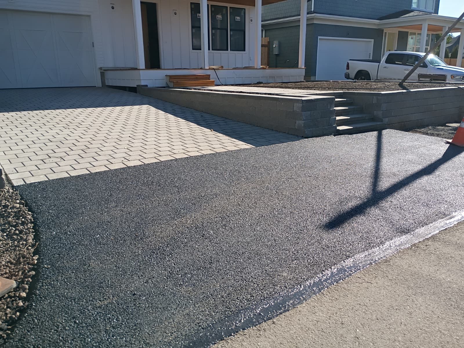 Front yard driveway with paver and asphalt surfaces beside a house and raised stone planter.