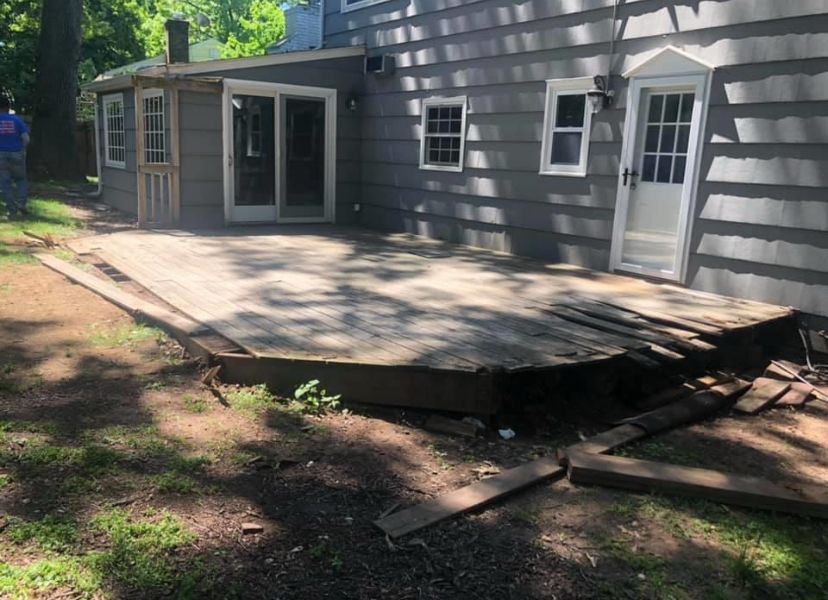 Collapsed wooden deck beside gray house with white-framed doors and windows