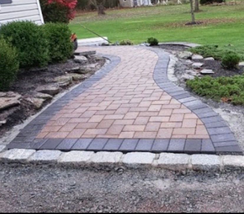 Curved brick garden walkway with gray border stones leading through a landscaped yard.