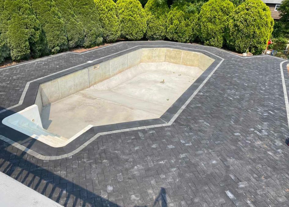 Empty hexagonal pool or pond surrounded by dark gray paving and green hedges.