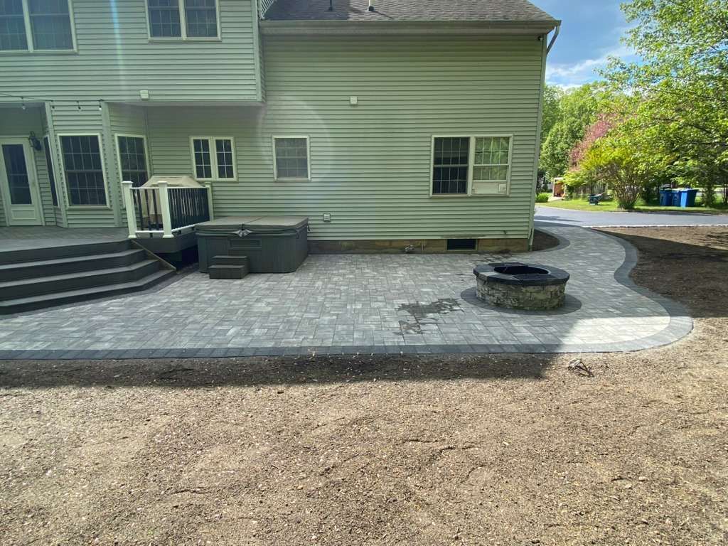 Backyard patio with gray pavers, steps, a grill, and a circular fire pit beside a beige house